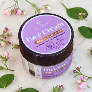 A jar of Marusha Rosehip Face Cream with Vege-Collagen and Rosehip oil, styled on a white marble surface with scattered rose petals and green leaves.