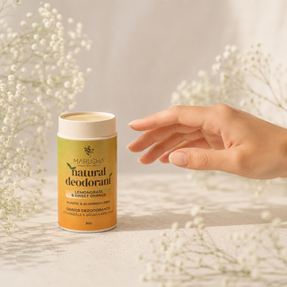 A hand reaches toward a jar of Marusha Natural Deodorant bar in Lemongrass & Sweet Orange, set against a soft, warm background