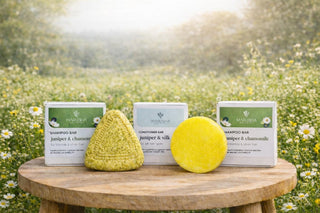 Marusha kadiķa un rozmarīna šampūnziepes un zīda cietais kondicionieris ar kastītēm uz koka galda ar pļavas ziediem aizmugurē