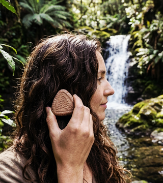 Sievietei ar brūniem matiem cietās šampūnziepes rokās pie upes dabā