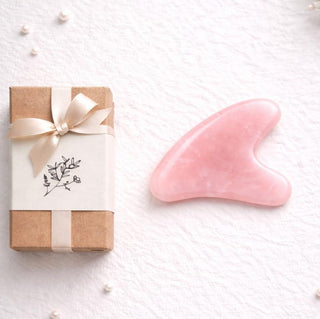 Pink gua sha tool next to a wrapped gift on a white textured surface