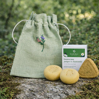 Green drawstring bag with embroidered design, two shampoo bars, and a packaging label on a natural background.