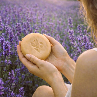Sieviete lavandu laukā tur rokās dabīgās Lavandas ziepes ar Kakao sviestu un rozā māliem