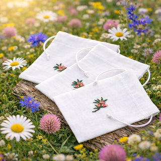 White face masks with floral embroidery on a wooden log surrounded by wildflowers