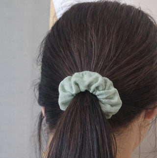 Green scrunchie on a person's ponytail against a neutral background