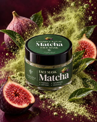 A jar of Marusha Matcha Face Mask is centered on a dark burgundy background, surrounded by fresh figs, green leaves, and a dramatic burst of matcha powder. The jar has a dark green label and a black lid.